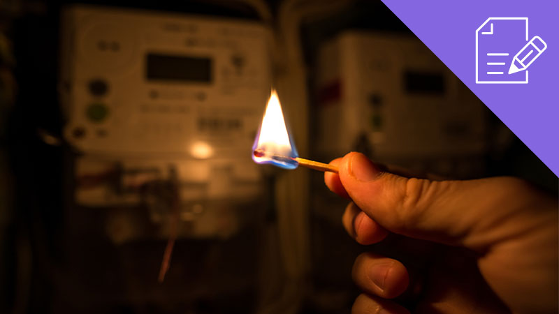Pessoa a segurar fósforo aceso no escuro junto a quadro elétrico